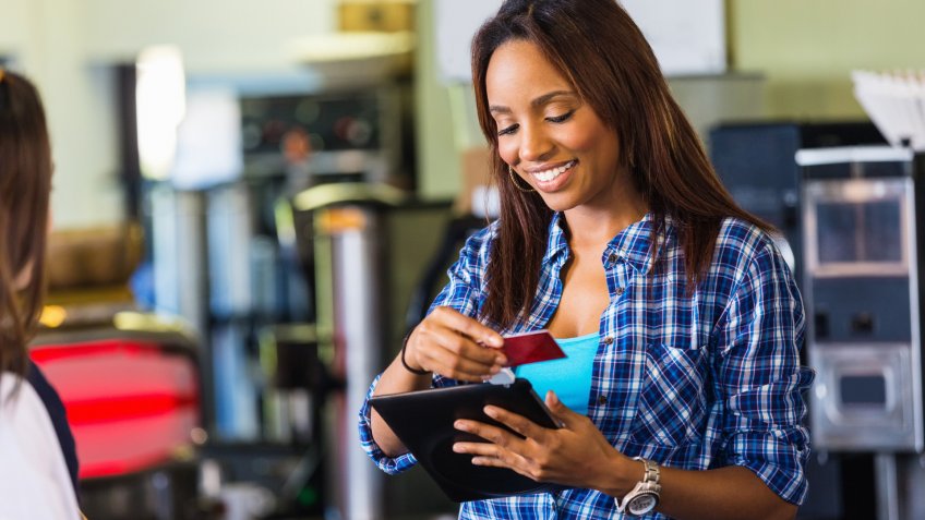 Coffee shop cashier swiping card on digital tablet reader.