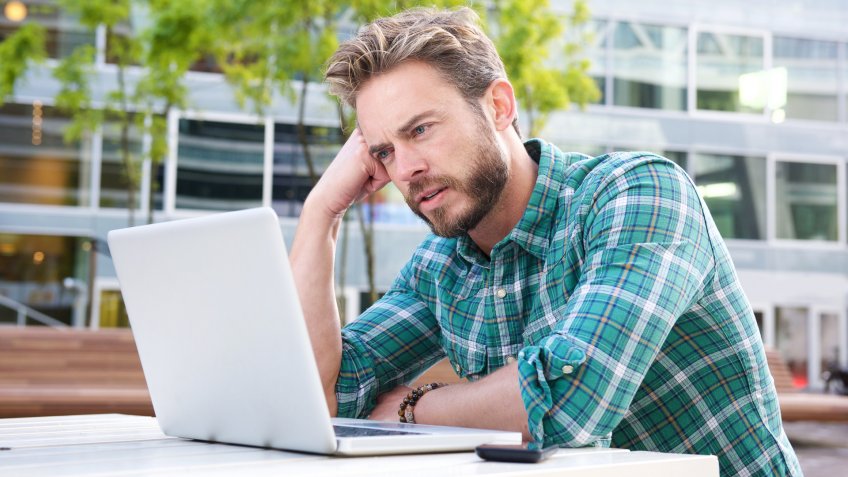 Portrait of a man sitting outside in the city with laptop.