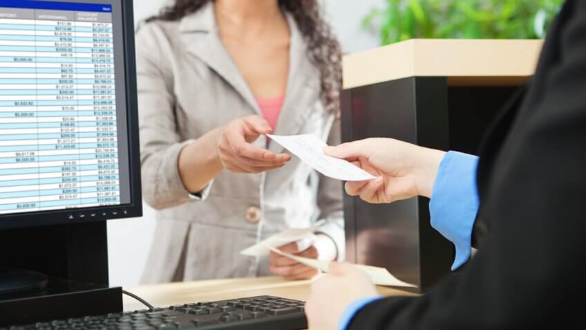 Over-the-shoulder shot of a transaction between a bank teller and a customer in a retail bank.