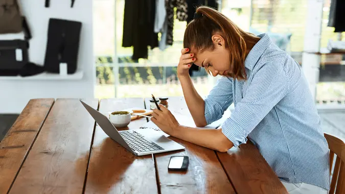 An anxious woman sitting at a table with her laptop and phone.