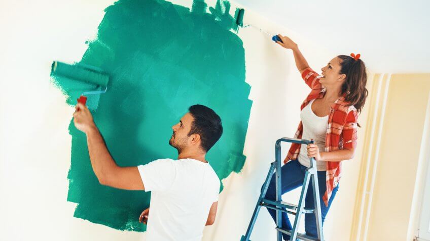 Closeup side view of a couple painting walls of their new apartment with paint rollers.