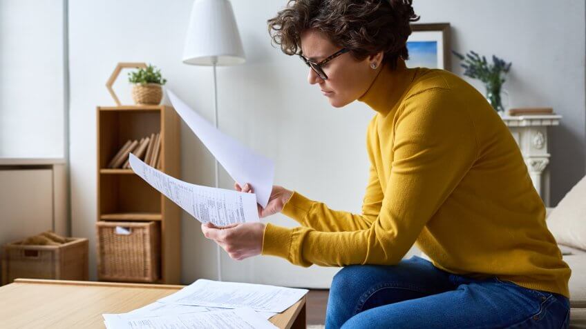 Concentrated woman reviewing financial documents at home.