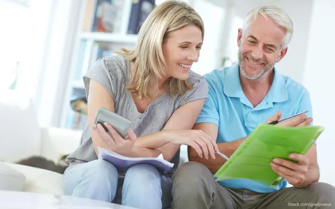 An older couple sits on the couch, reviewing their retirement savings in a green folder.