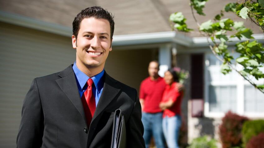 realtor posing for a picture with homeowners in the background realtor posing for a picture with homeowners in the background
