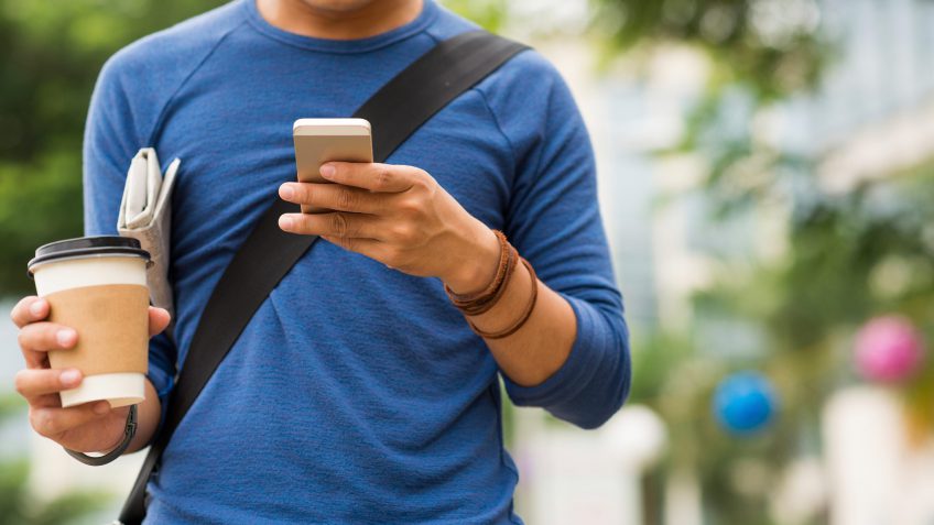 young man looking at his phone while holding a cup of coffee
