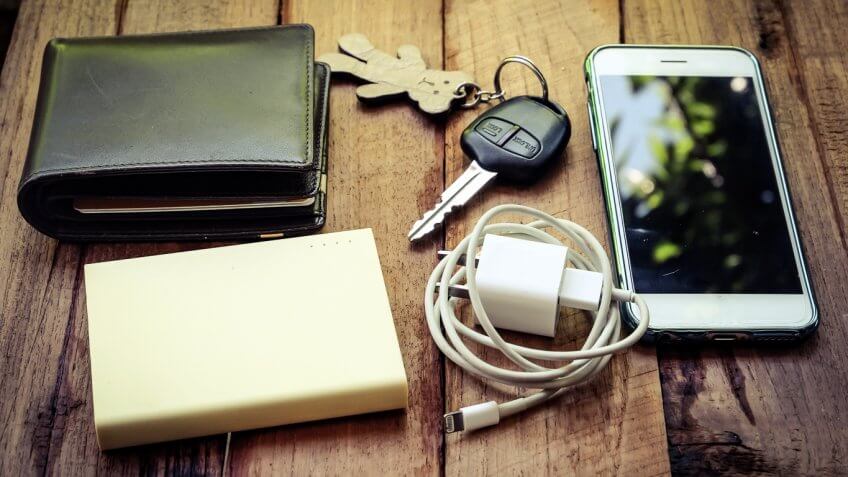 wallet, battery pack, iphone cord, iphone, charger, keys on a table