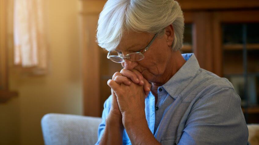 senior woman looking worried with her hands clasped together at home