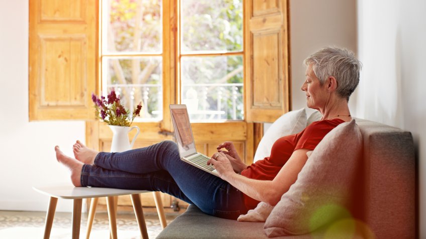 mature woman relaxing on her sofa at home using a laptop