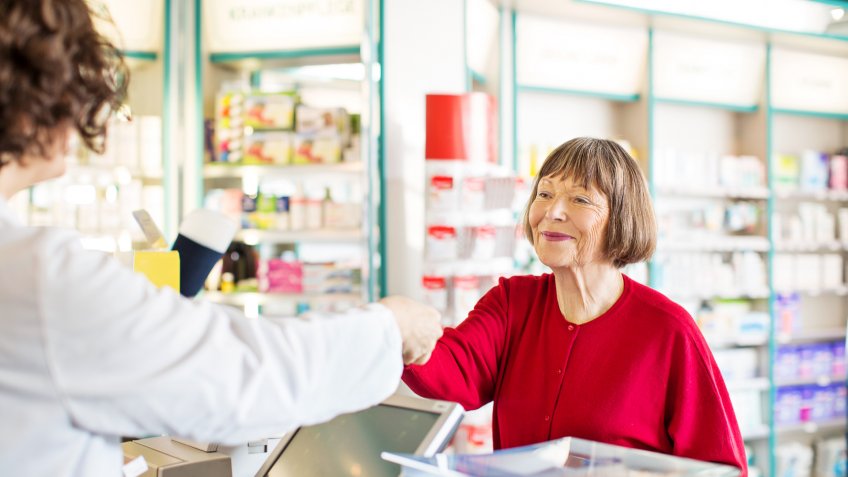 Senior female customer standing at chemist counter as pharmacist hands her medication order.