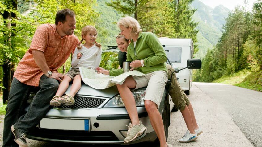 family with two children sitting on their car in nature during a road trip