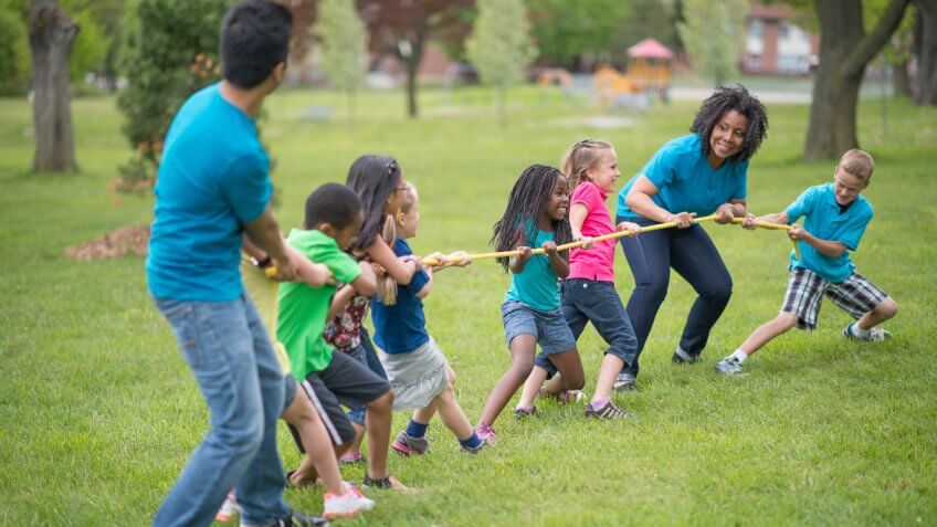 children and two adults playing tug o war summer camp games