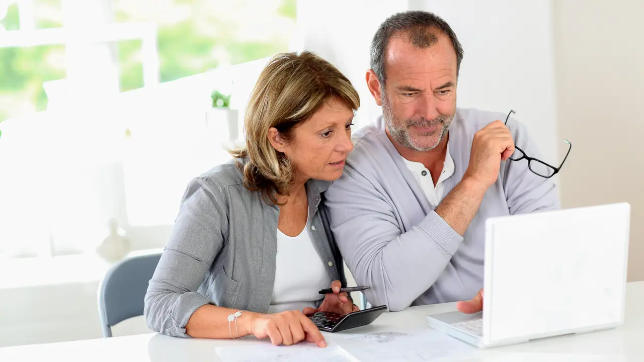 Shot of a couple sitting at a white table together and discussing their finances displayed on a laptop