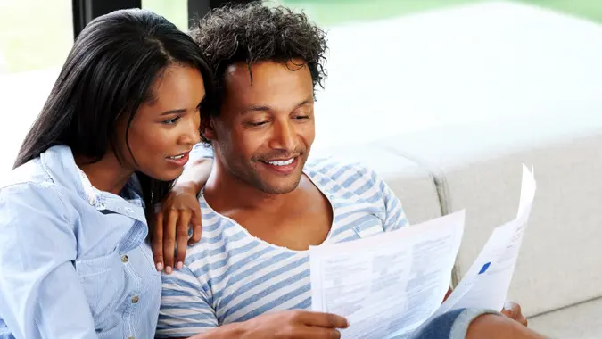 Young couple sitting on sofa reading a financial bill at home.