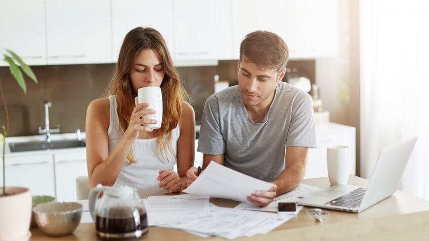 Handsome man sitting near his wife at kitchen, showing her important document.