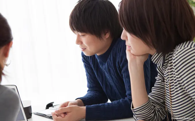 Couple in a meeting with a financial advisor, appearing concerned while reviewing financial paperwork.