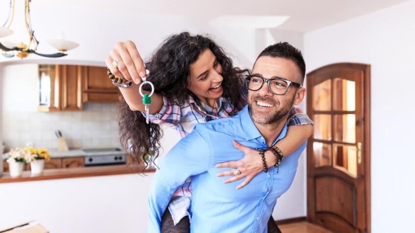 Young couple moving in new apartment, holdinh keys, in piggyback ride.