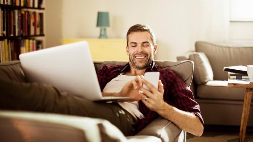 Photo of a handsome mature man lying on sofa and texting on his smart phone.
