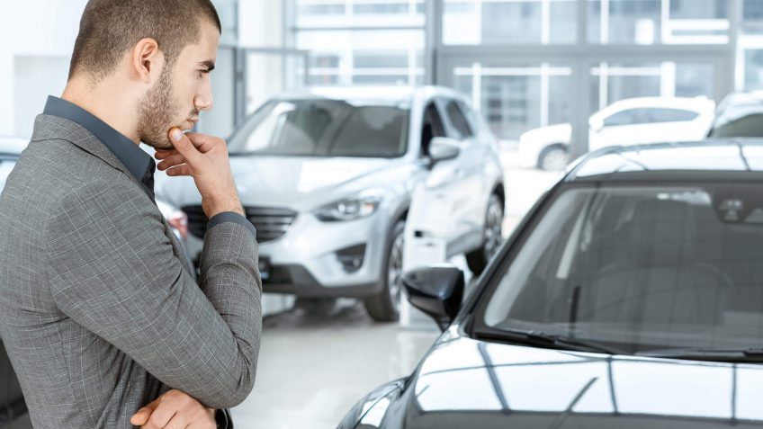 young man looking at a new car in thought