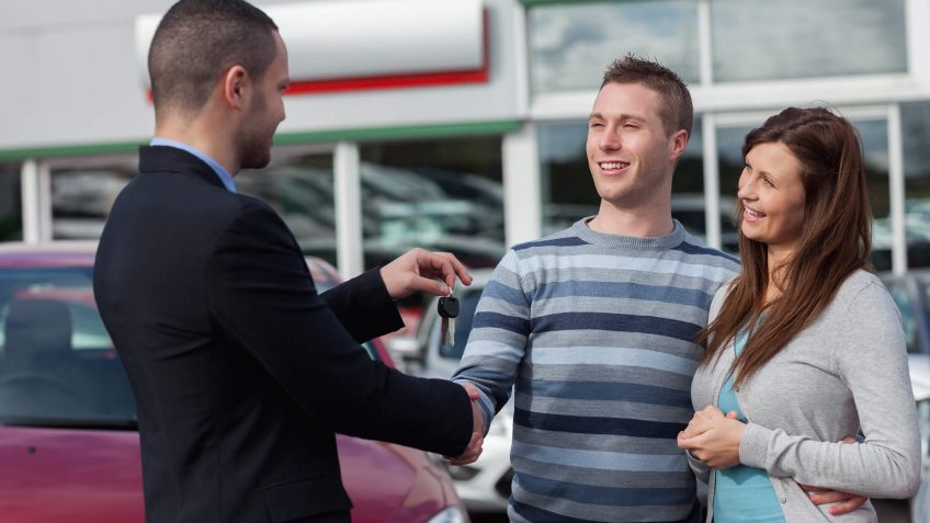 smiling couple receiving keys to their new car