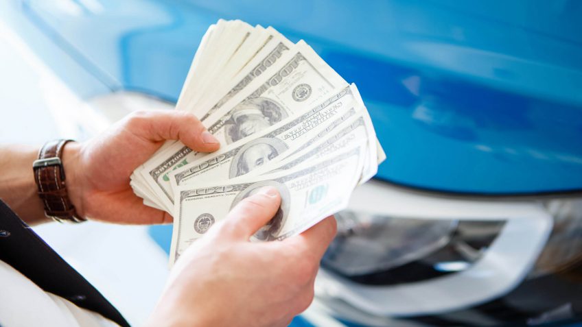 man holding a fan of cash at a car dealership