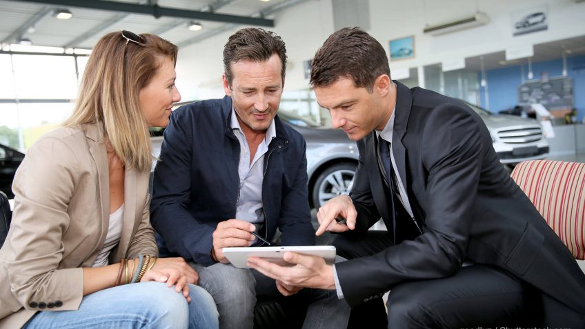 car salesman showing a couple information on a tablet