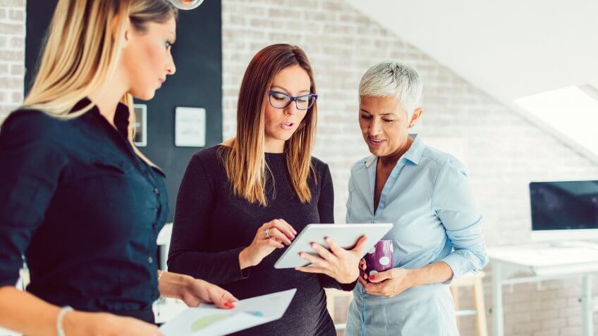 Two young businesswoman standing in their office and talking with their mentor, mature businesswoman.