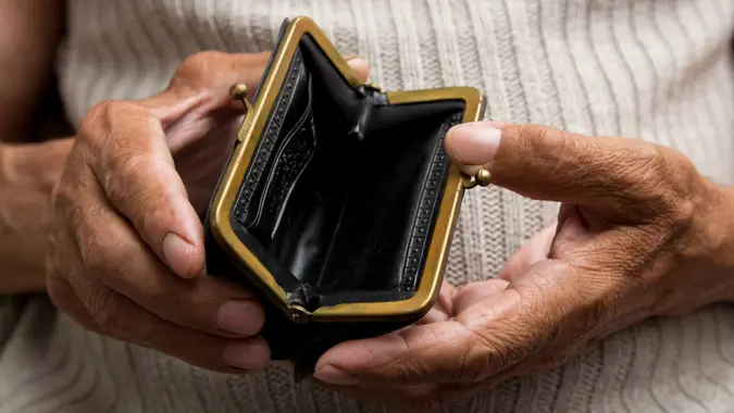 An elderly man holds an empty purse.