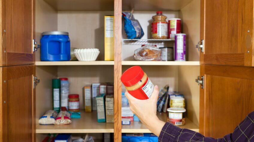 Close up of a woman's hand taking a jar of peanut butter out of an open pantry.