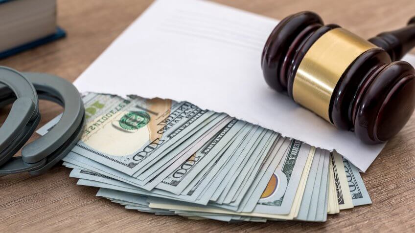 Biggest Money Scams of All Time, Handcuffs, corruption. dollars in an envelope, gavel and book judge.