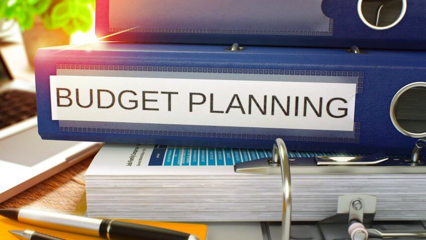 Blue Ring Binder with Inscription Budget Planning on Background of Working Table with Office Supplies and Laptop.