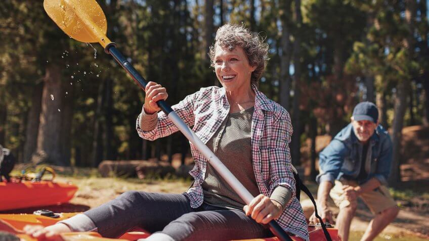 Portrait of happy senior paddling kayak in the lake with man supporting from behind.