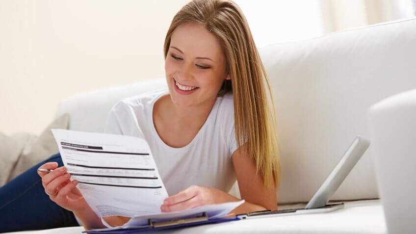 Happy young girl with laptop computer calculating bills in living room.