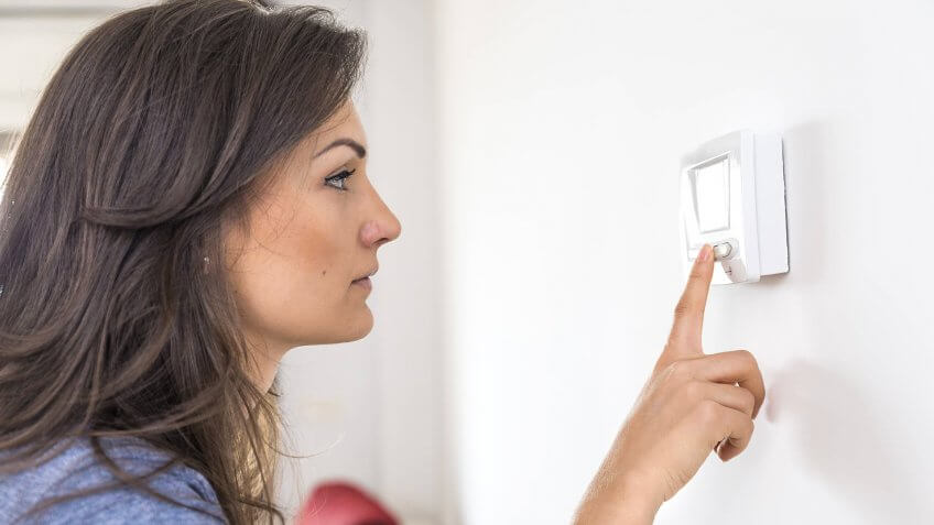 Beautiful woman push button digital thermostat at house.