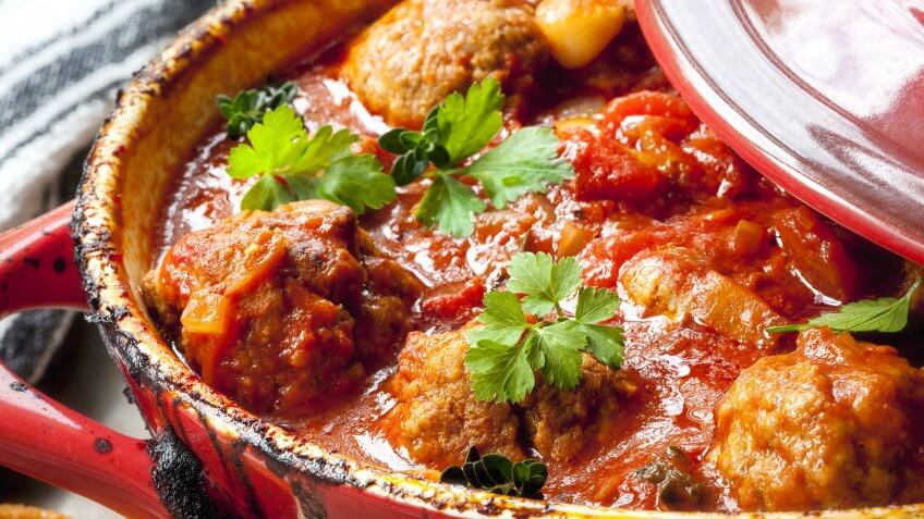 Chicken meatballs in tomato sauce, cooking in red casserole dish.