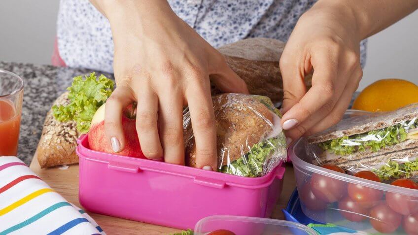 A closeup of hands packing snacks into a pink lunch box.