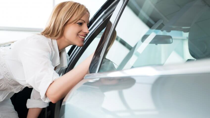 Mid adult woman looking through a opened window of a car in a showroom.
