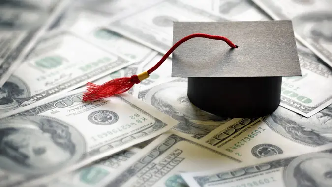 Graduation mortar board cap on one hundred dollar bills concept for the cost of a college and university education.