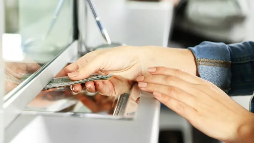 woman giving her money to someone behind a teller window