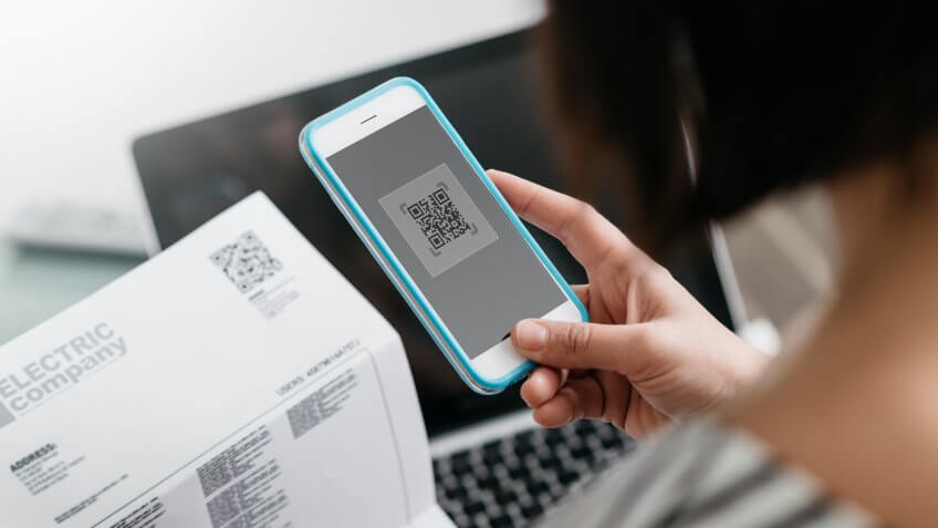 Woman checking an electricity bill, she is making a contactless payment using her smartphone.