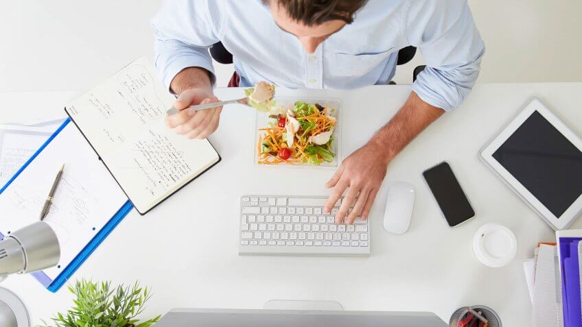 Overhead View Of Businessman Working At Computer In Office Eating Lunch.