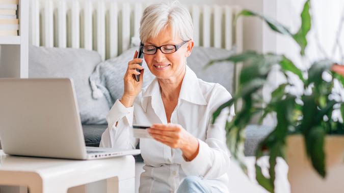 Happy Mature woman sitting on floor in her living room and using laptop for online banking, online shopping or just fun.