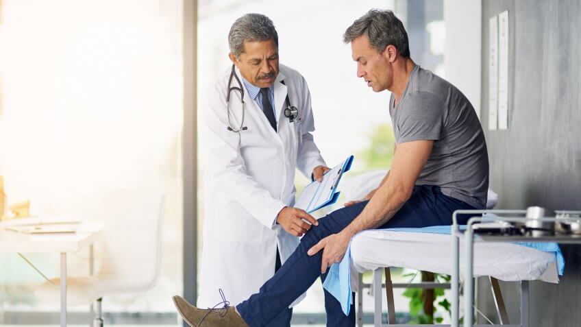 Shot of a mature doctor examining his patient who is concerned about his knee.
