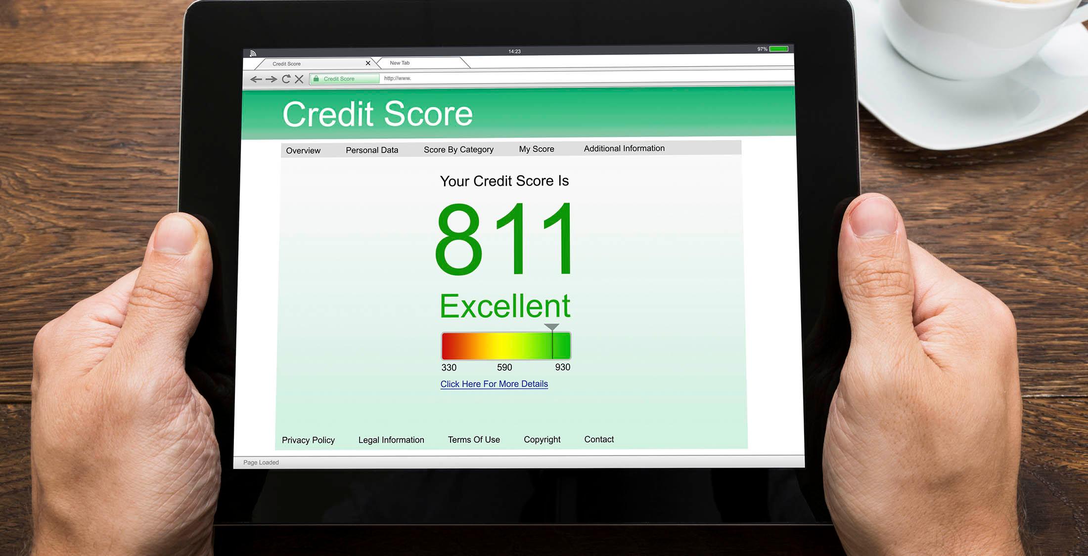 Close-up Of Person Hands With Digital Tablet Showing Credit Score At Desk