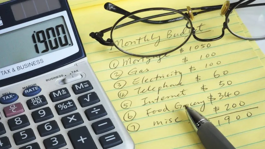 monthly budget notepad with glasses, pen and calculator on top