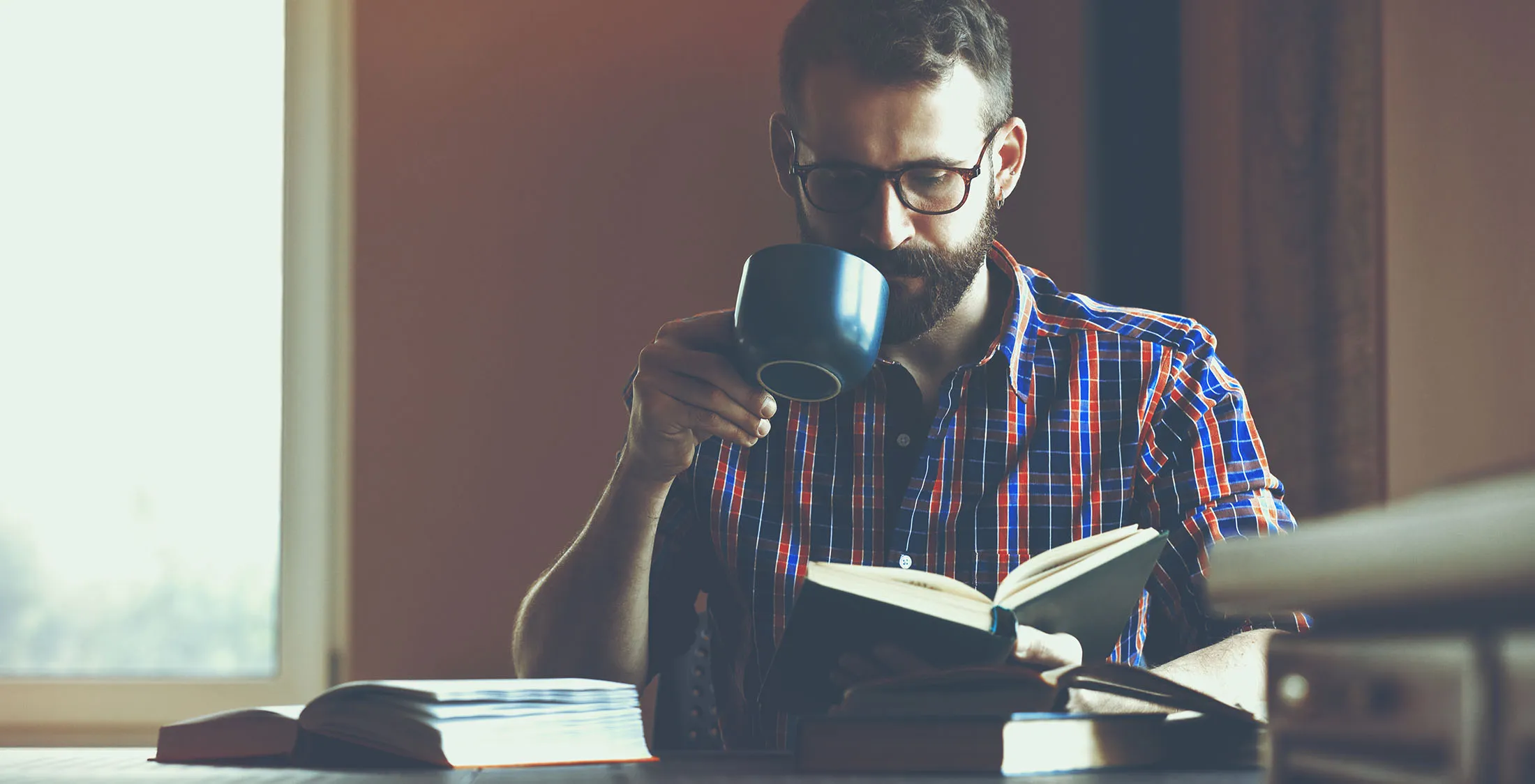 man sipping on coffee and reading a book
