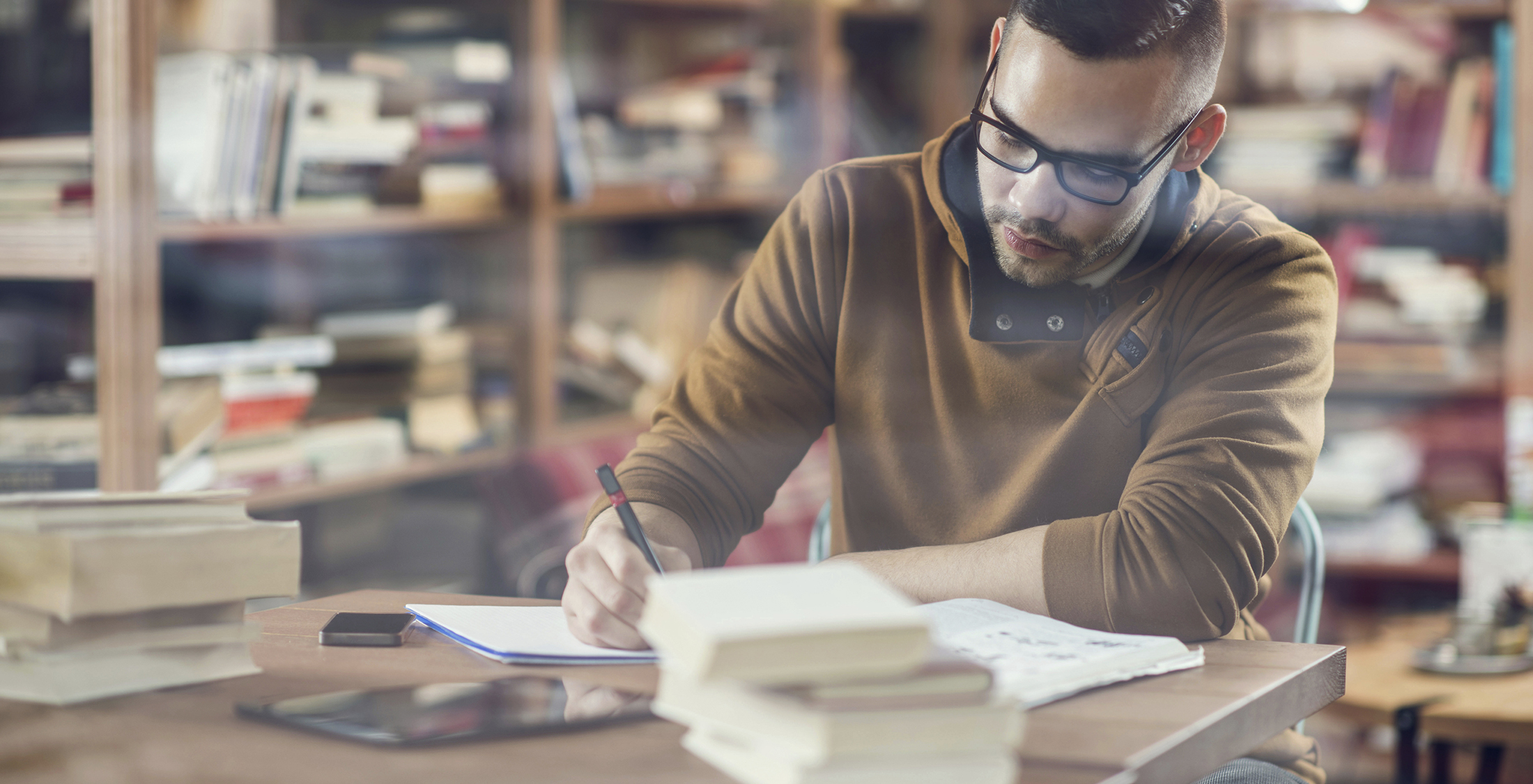 Buy used textbooks. Young male student taking notes for his exams in library.