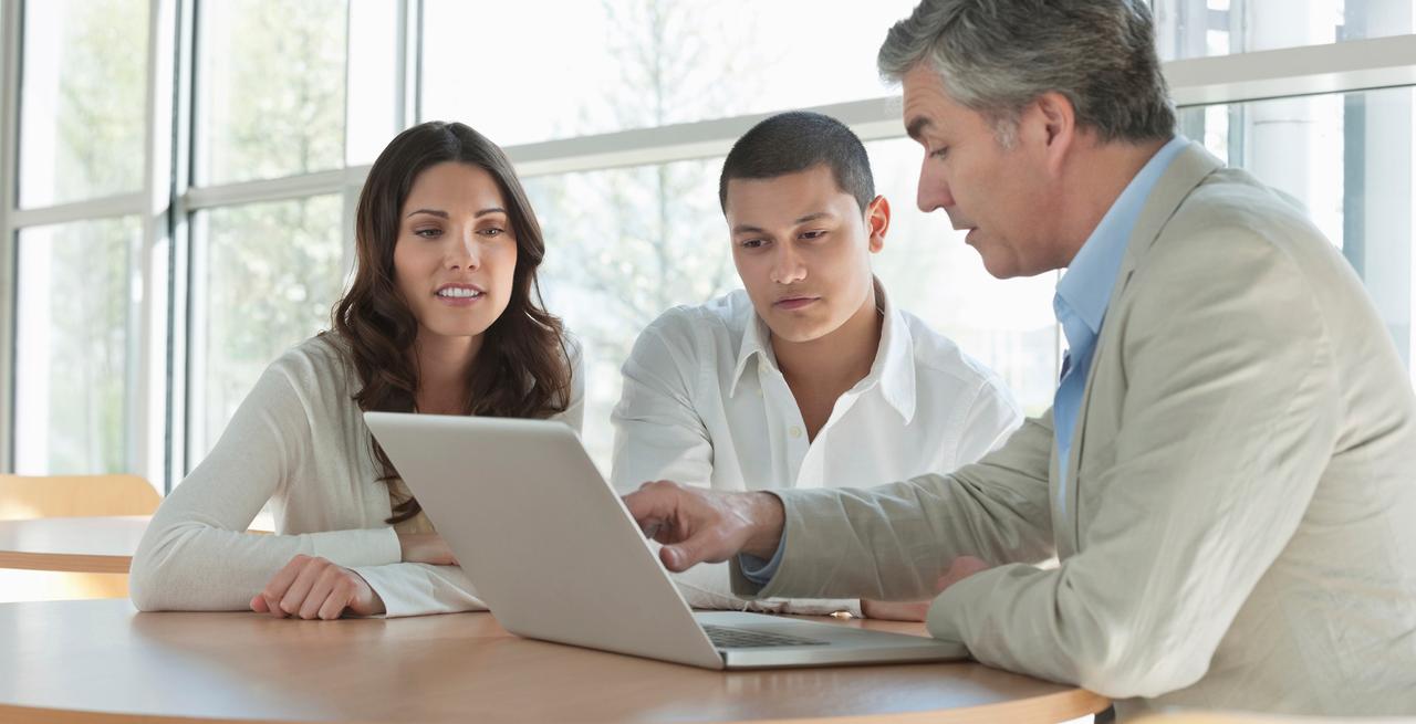 Mature financial advisor explaining an investment scheme on laptop to young couple