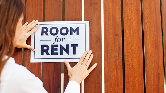 woman attaching a "room for rent" ads on a wooden wall.