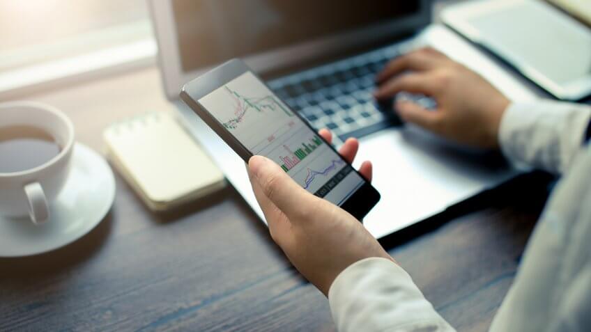 Hand holding smartphone with stock graph.