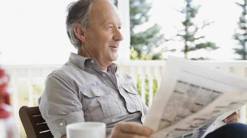 Senior man reading newspaper on porch.